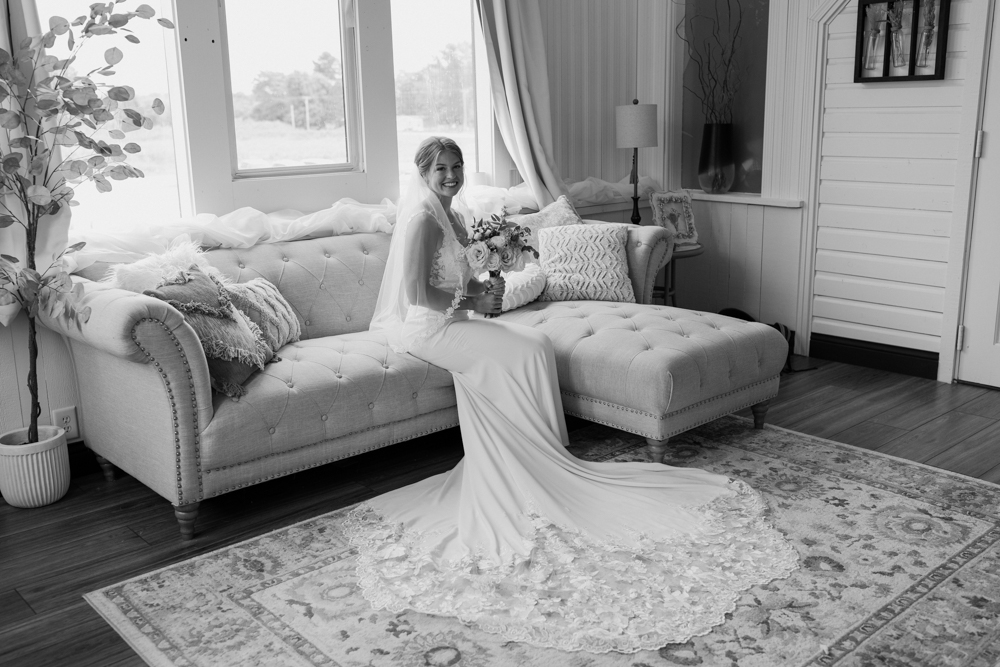 A bride sits on a couch with her wedding dress, purchased from Atlas Bridal in Toledo, flared out on the carpet