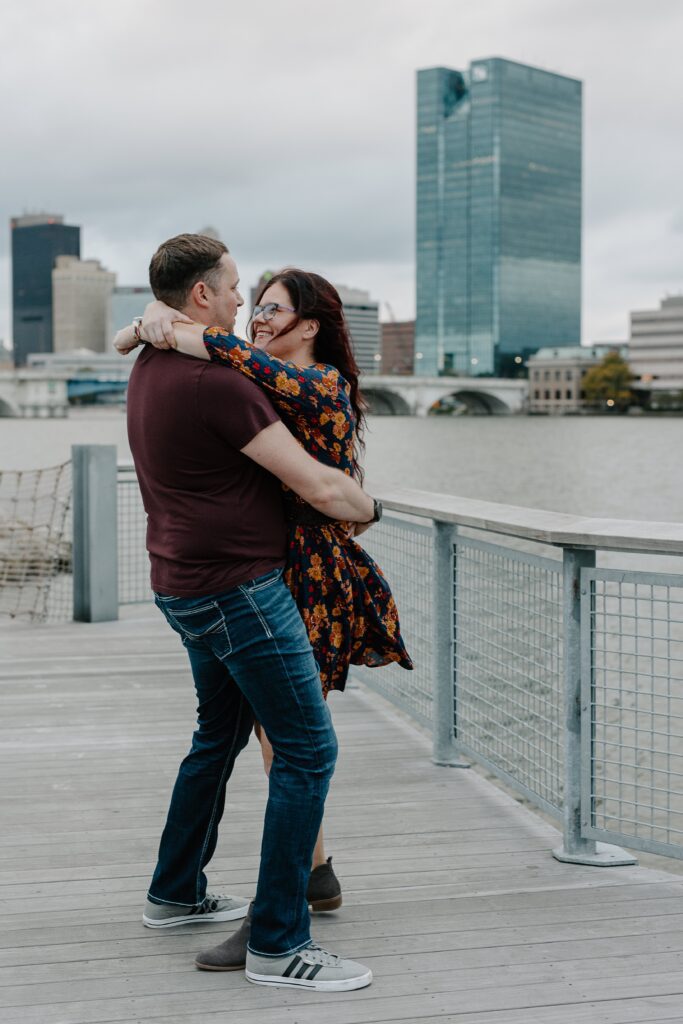 A couple embraces during engagement photos at Glass City Metropark along the river walk